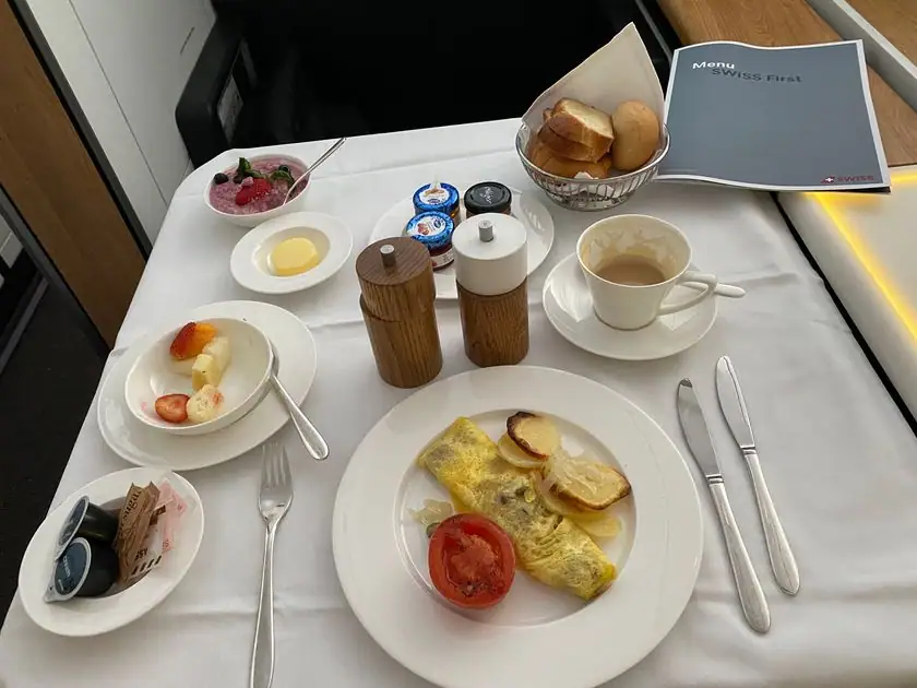 Gedecktes Frühstück in der Swiss First Class: Omelette, Aufschnitt, Brot und Kaffee auf weißem Leinen