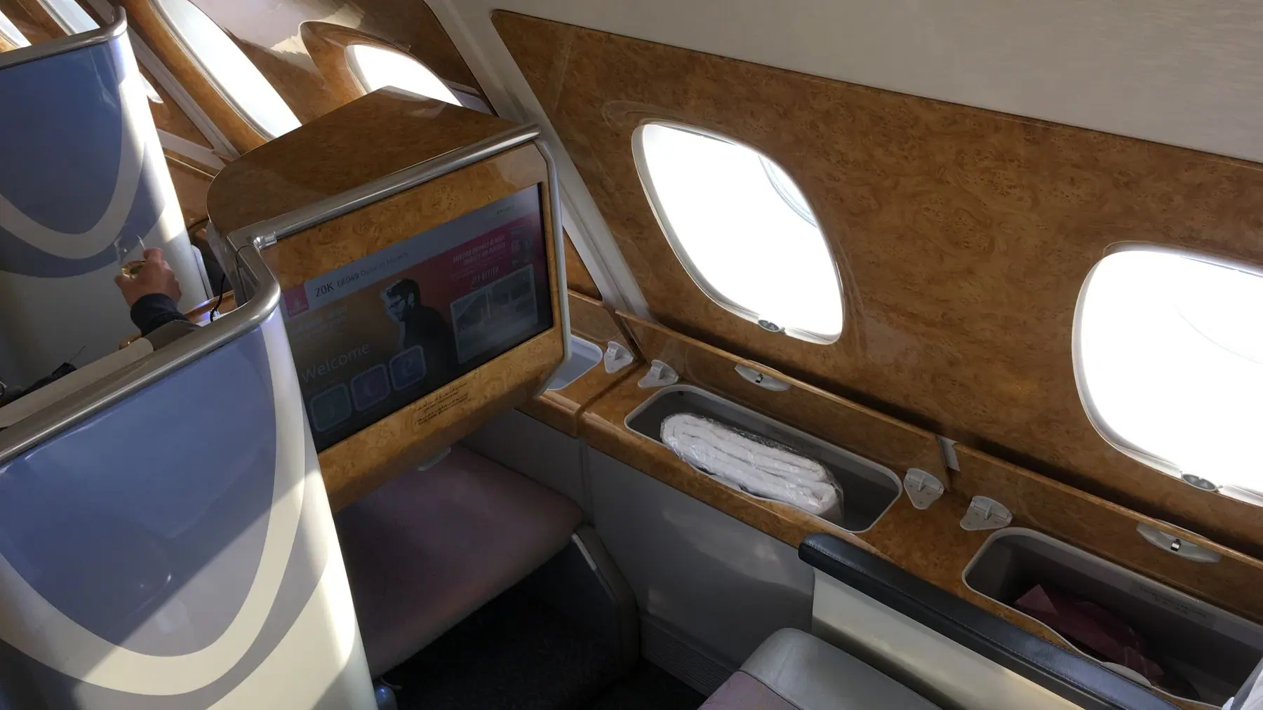 Blick in eine Emirates Business Class Kabine im A380 mit Wurzelholz und beleuchteten Bildschirmen