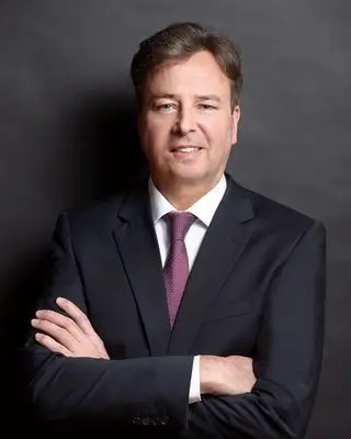 Andreas I. im dunklen Anzug vor grauem Hintergrund
