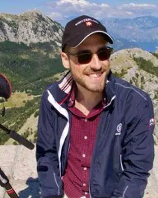 Lars Fliegner mit Mütze und Sonnenbrille auf einem Berggipfel